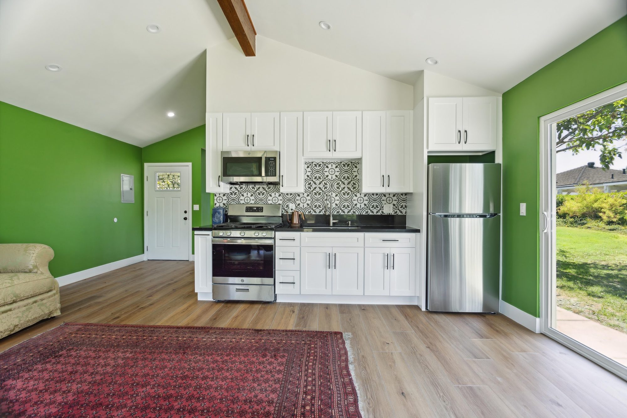 Open living space and kitchen finished as part of a room addition, with vaulted ceiling, exposed beam, and slider door to the yard