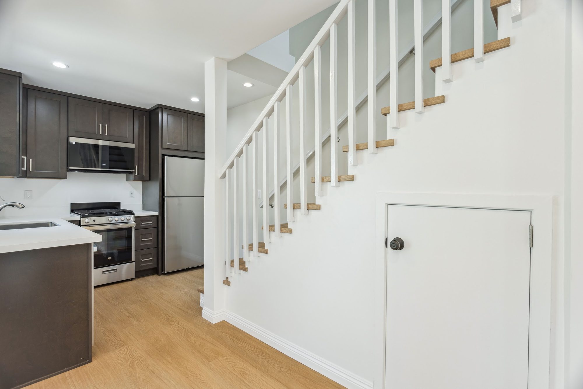 New interior staircase with white balusters leading to an added second-story addition, with a kitchen visible at the base