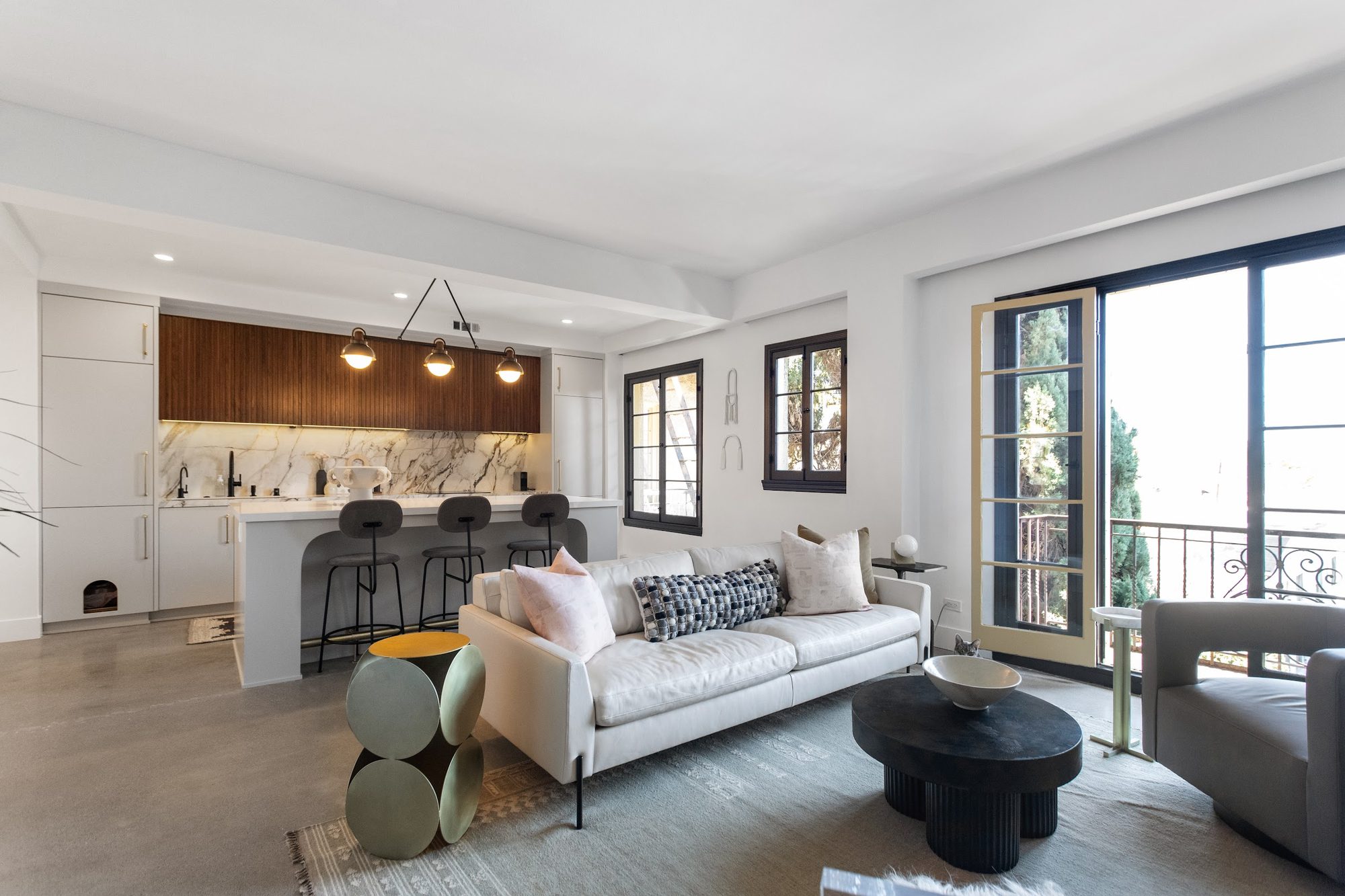 Open-concept luxury kitchen and living space with walnut cabinetry, waterfall marble backsplash, and French doors to a balcony